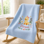 May include: A light blue knitted baby blanket featuring an embroidered design of a yellow duckling with a pink bow, surrounded by white daisies, green reeds, and small yellow stars. The name Harper is embroidered in pink cursive script bel